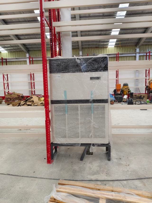 Large industrial air conditioner wrapped in plastic, positioned on a metal stand inside a warehouse.