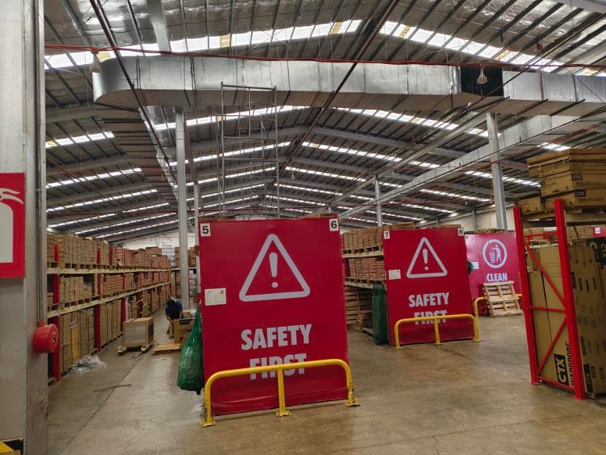 Large red 'Safety First' signs stand in a warehouse with high ceilings and storage shelves.
